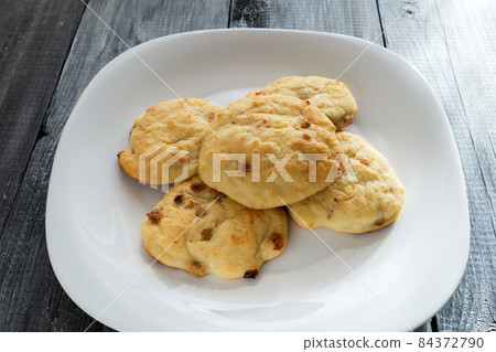 Dessert from cottage cheese with raisins. Cottage cheese pancakes baked in the oven in a white plate on a wooden background. Dessert from cottage cheese with raisins. Cottage cheese pancakes baked in the oven in a white plate on a wooden background. 84372790
