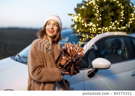Happy woman with gifts and Christmas tree outdoors Happy woman with gifts and Christmas tree outdoors 84373351