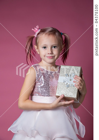 Little caucasian girl in a festive dress with sequins posing holding gift box Little caucasian girl in a festive dress with sequins posing holding gift box 84378100