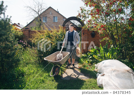 A man carries a garden wheelbarrow for loading sand to fill the paths 84378345