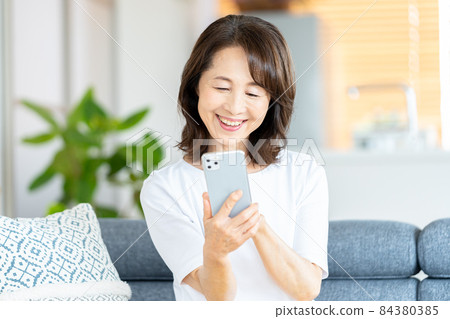 Senior woman operating a smartphone in the living room Senior woman operating a smartphone in the living room 84380385