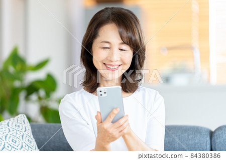 Senior woman operating a smartphone in the living room Senior woman operating a smartphone in the living room 84380386