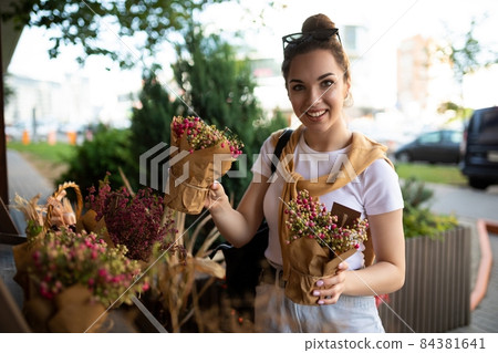 Young positive happy beautiful pretty brunette woman enjoying flowers in pots on the porch of a 84381641