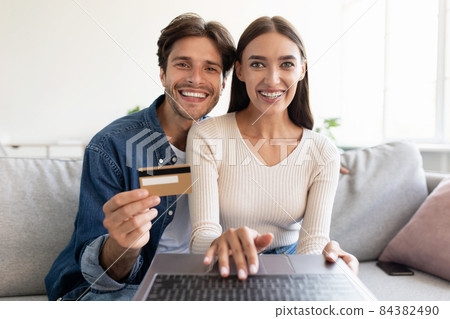 Cheerful european young family with laptop look at webcam and make online purchases with credit card 84382490