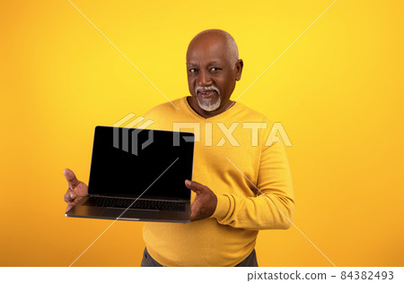 Portrait of happy senior black man demonstrating laptop with empty screen, posing on orange studio background, mockup Portrait of happy senior black man demonstrating laptop with empty screen, posing on orange studio background, mockup 84382493