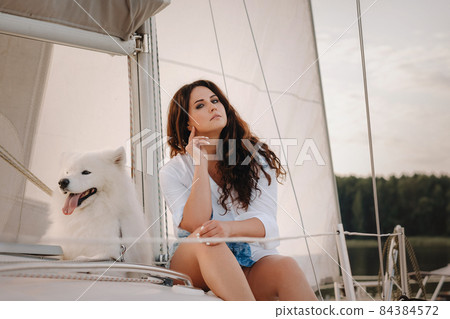 a happy woman with a big white dog on a white yacht in the sea 84384572