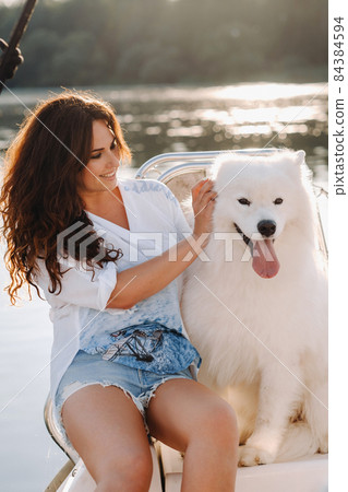 a happy woman with a big white dog on a white yacht in the sea 84384594