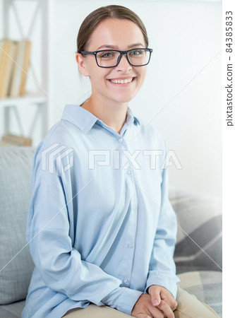 Intelligent woman portrait. Success motivation. Psychotherapy wellbeing. Confident cheerful smiling smart female mentor in eyeglasses on couch at light home interior. Intelligent woman portrait. Success motivation. Psychotherapy wellbeing. Confident cheerful smiling smart female mentor in eyeglasses on couch at light home interior. 84385833