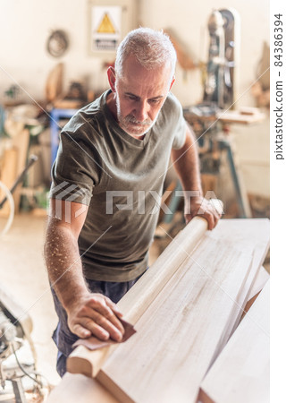 Mature carpenter man standing carefully sanding wood 84386394