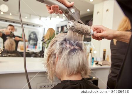 Male hairdresser blow drying client hair with round brush Male hairdresser blow drying client hair with round brush 84386458