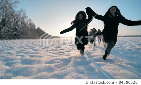 Cheerful girls run across the snow-covered field. Cheerful girls run across the snow-covered field. 84386526