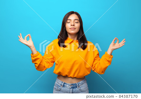 Breathe in. Beautiful multiethnicity woman in orange shirt getting zen calm against blue background 84387170