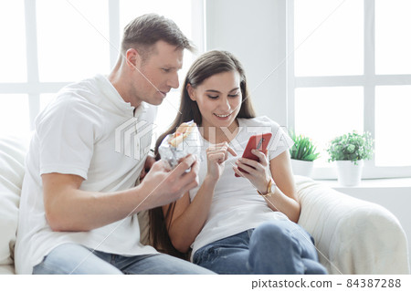 young couple with a smartphone sitting on a comfortable sofa. young couple with a smartphone sitting on a comfortable sofa. 84387288