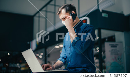 young man in a protective mask is choosing a contact in his smartphone 84387397