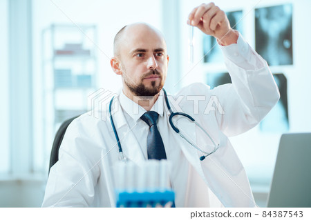 young scientist looks at an ampoule with a vaccine. young scientist looks at an ampoule with a vaccine. 84387543