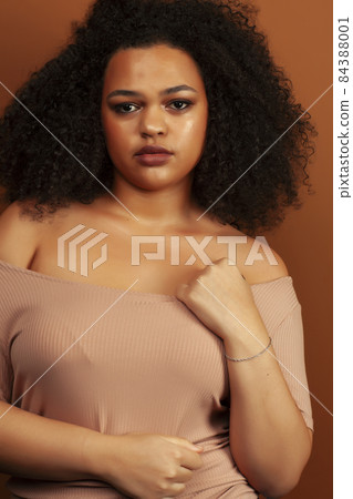 pretty young african american woman with curly hair posing cheerful gesturing on brown background, lifestyle people concept 84388001