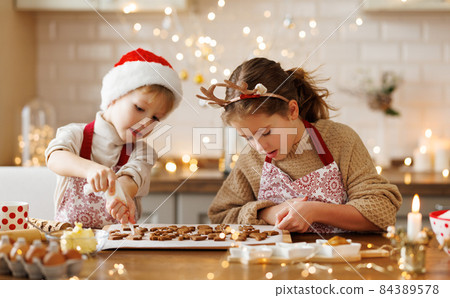 Happy children boy and girl smiling while decorating Christmas gingerbreads in kitchen 84389578