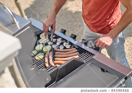A man in red shirt standing near the barbecue grill and cooking veggies A man in red shirt standing near the barbecue grill and cooking veggies 84390488