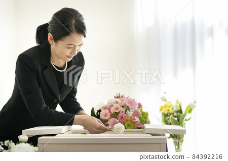 A woman in mourning who puts flowers in a casket A woman in mourning who puts flowers in a casket 84392216