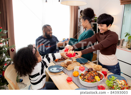 Happy family with daughter giving gift box with father and mother during dinner at home. Happy family with daughter giving gift box with father and mother during dinner at home. 84393003