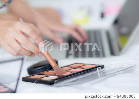 Hands of woman with learning makeup with brush on cheek on laptop computer with tutorial course. 84393005
