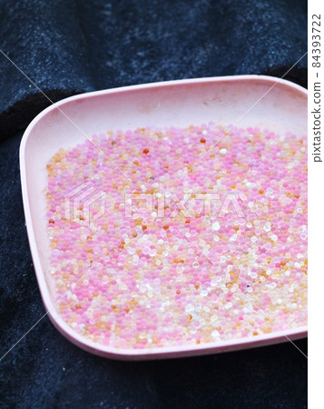 used pink coloured blue silica gel from a camera lens keeping box in plastic dish on house roof in sun drying process for reuse 84393722