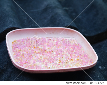 used pink coloured blue silica gel from a camera lens keeping box in plastic dish on house roof in sun drying process for reuse 84393724