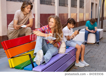Group of teenagers sitting on bench outdoors 84393936