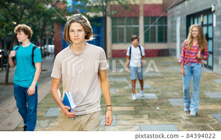 Teen boy walk along summer street after finishing college lessons Teen boy walk along summer street after finishing college lessons 84394022