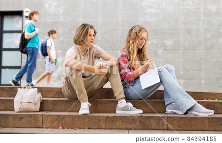 Teenage boy and girl sitting on steps near school Teenage boy and girl sitting on steps near school 84394185
