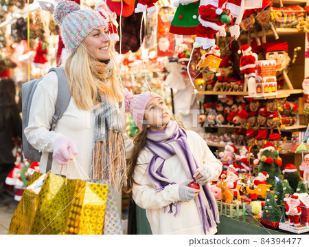 Mom and daughter point to Christmas decorations, choose and buy at Christmas market Mom and daughter point to Christmas decorations, choose and buy at Christmas market 84394477