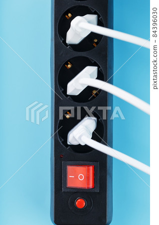 A black mains filter with electrical outlets inserted into it with white plugs of electrical appliances on a blue background A black mains filter with electrical outlets inserted into it with white plugs of electrical appliances on a blue background 84396030