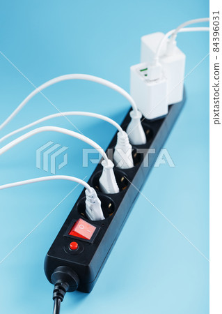 A black mains filter with electrical outlets inserted into it with white plugs of electrical appliances on a blue background 84396031