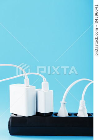 A black mains filter with electrical outlets inserted into it with white plugs of electrical appliances on a blue background 84396041