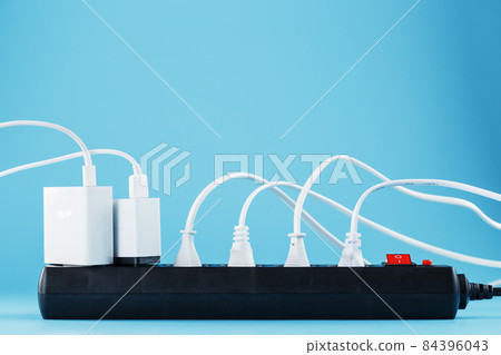 A black mains filter with electrical outlets inserted into it with white plugs of electrical appliances on a blue background 84396043