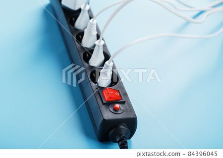 A black mains filter with electrical outlets inserted into it with white plugs of electrical appliances on a blue background 84396045