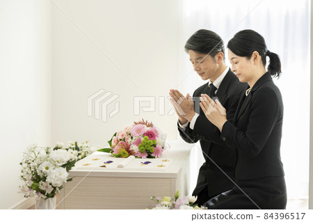 Men and women in mourning clothes holding hands in front of the casket 84396517