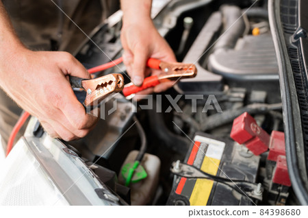 The mechanic connects the clamps to the discharged car battery. The mechanic connects the clamps to the discharged car battery. 84398680