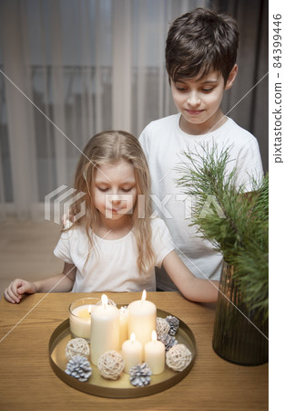 Children - a boy and a girl blow out Christmas candles at home in the evening. Children - a boy and a girl blow out Christmas candles at home in the evening. 84399446