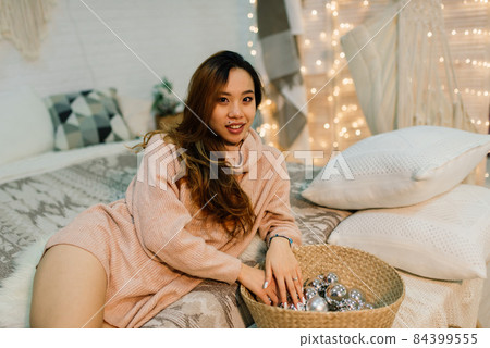 Pensive young pretty asian woman with burning candles on Christmas eve making wish 84399555