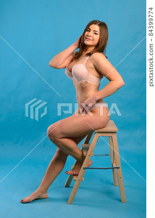 Beautiful emotional plus-size female model in pink and black bodysuit posing on background in studio 84399774