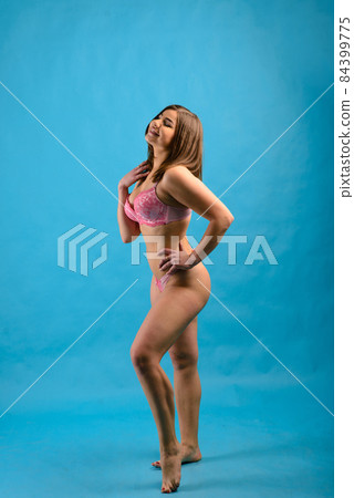 Beautiful emotional plus-size female model in pink and black bodysuit posing on background in studio 84399775
