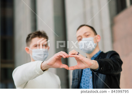 Young gay couple wearing medical mask, hugging and kissing at the city. 84399795