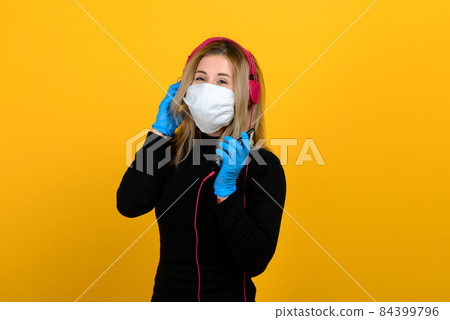 Portrait of a girl in a medical mask, which puts on a rubber glove. Yellow and grey background. Portrait of a girl in a medical mask, which puts on a rubber glove. Yellow and grey background. 84399796