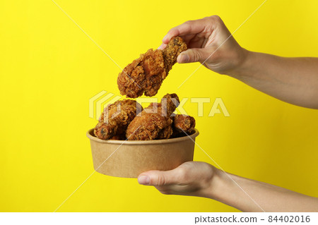 Female hands hold fried chicken on yellow background Female hands hold fried chicken on yellow background 84402016