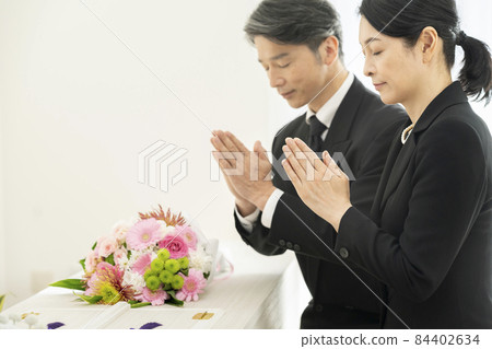 Men and women in mourning clothes holding hands in front of the casket Men and women in mourning clothes holding hands in front of the casket 84402634