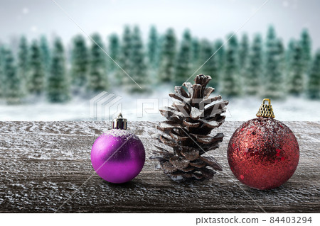 Wooden table with Christmas ball and a pine cone with a view of snowy fir trees 84403294