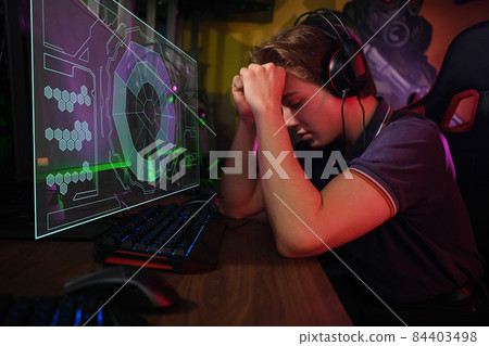 Professional young caucasian gamer playing online on his PC. He upset because of losing the game 84403498