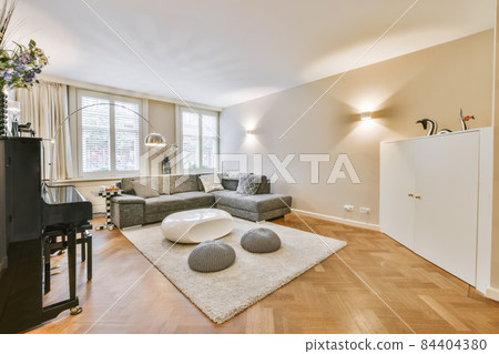 Comfortable sofa and armchair placed on soft carpet near windows in cozy light living room in modern flat 84404380