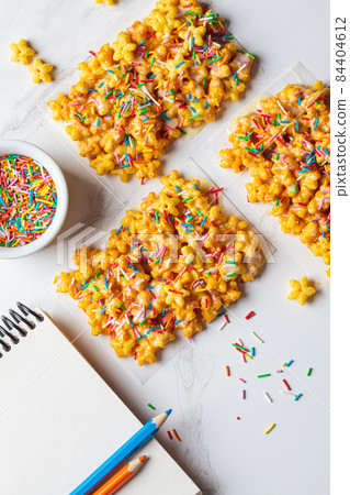 Children corn stars cereal bars with colored sprinkles and white chocolate on a white background. Children corn stars cereal bars with colored sprinkles and white chocolate on a white background. 84404612